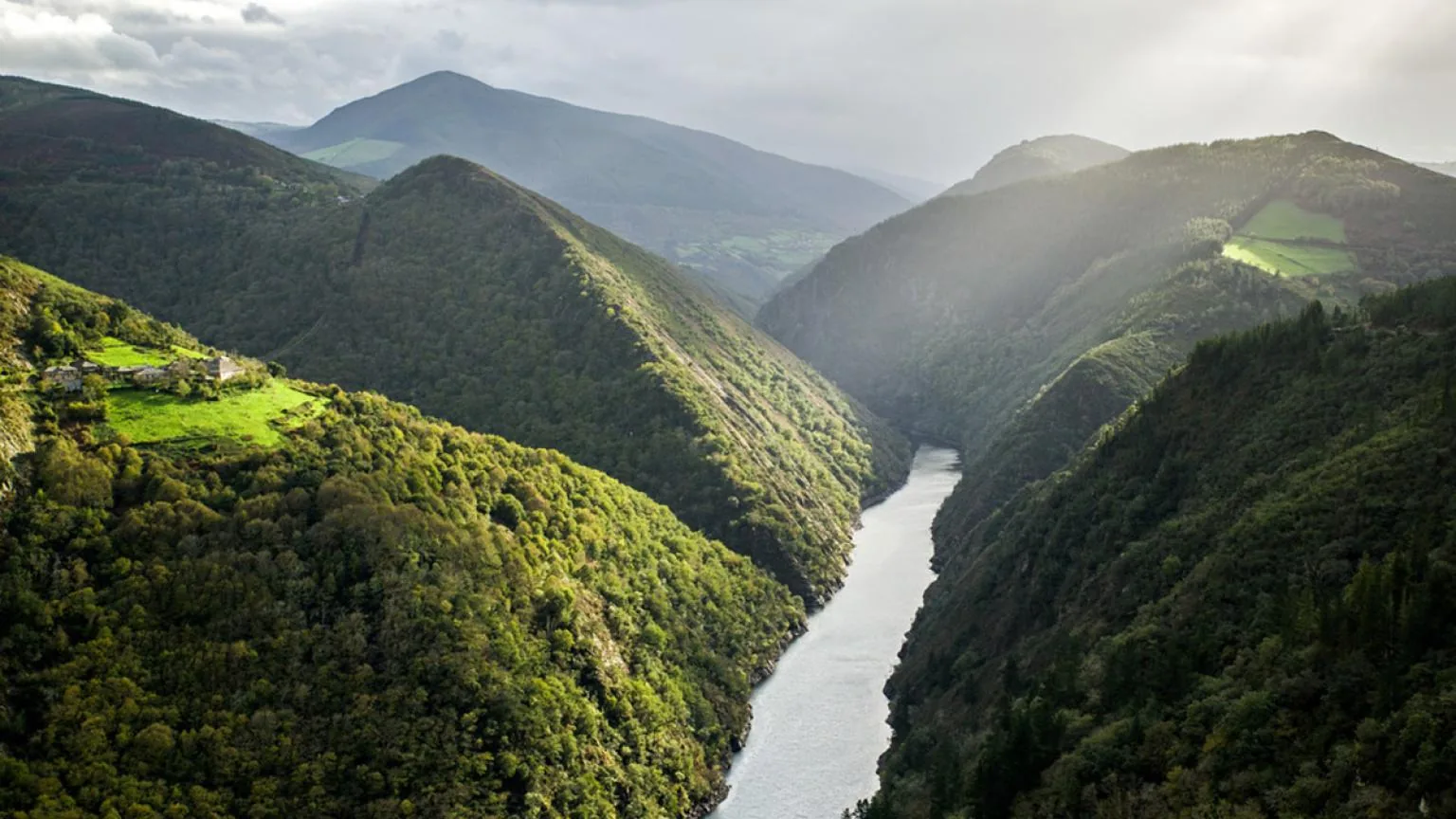 Valle de montaña cubierto de bosque, con un río encajado al fondo